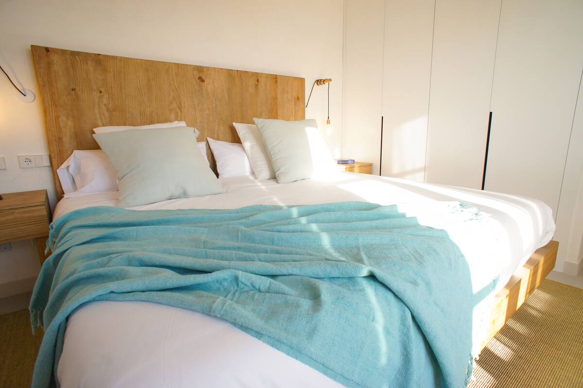 A neatly made bed with a blue blanket, wooden headboard, and white bedding.