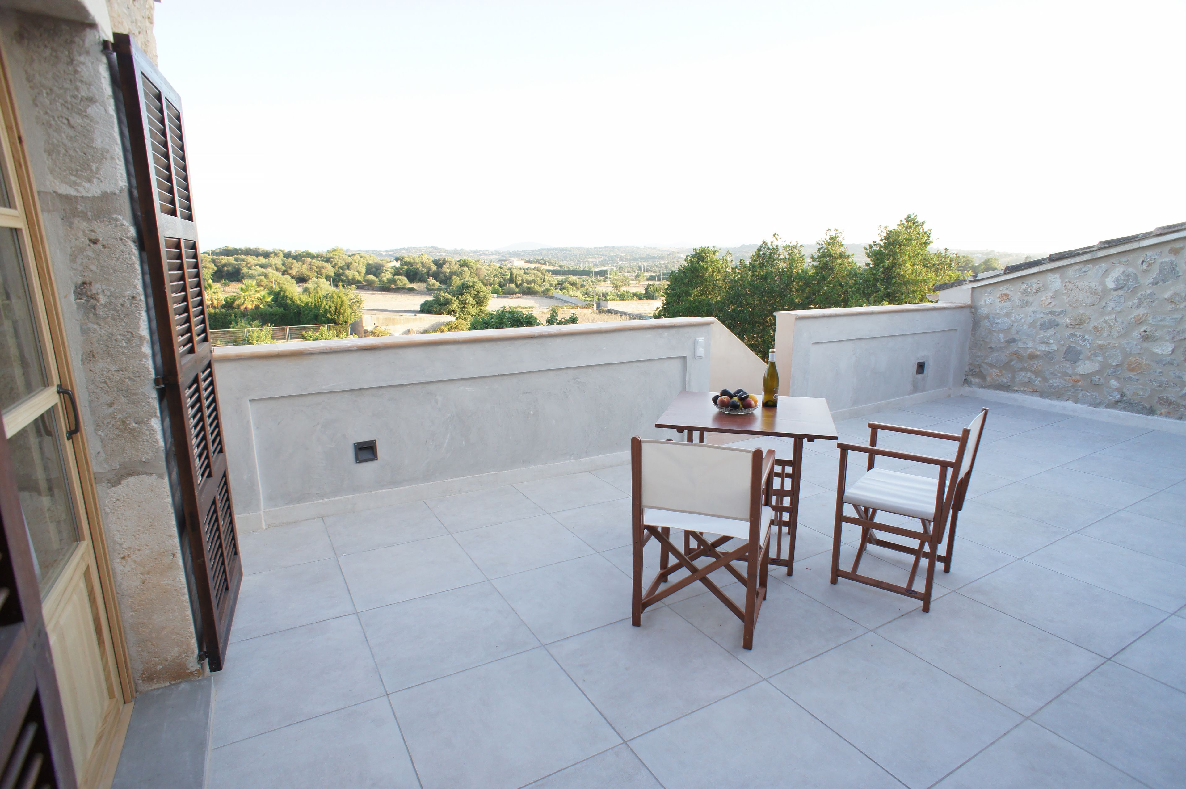 Een terras op het dak met een tafel en stoelen, uitzicht op het platteland en een stenen muur.