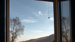 Una ventana con vista a un paisaje montañoso y un edificio con tejados de tejas rojas.