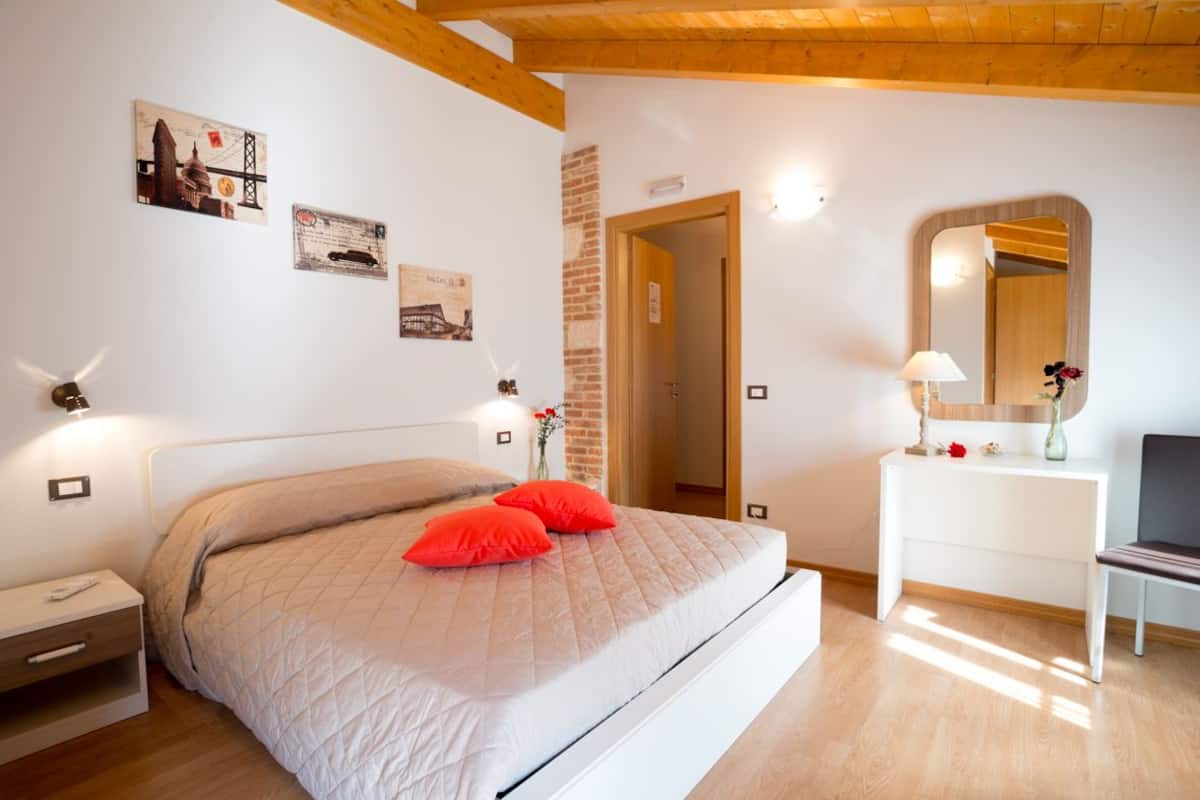 A bedroom with a bed, bedside table, nightstand, dresser, mirror, and wall-mounted light fixtures.