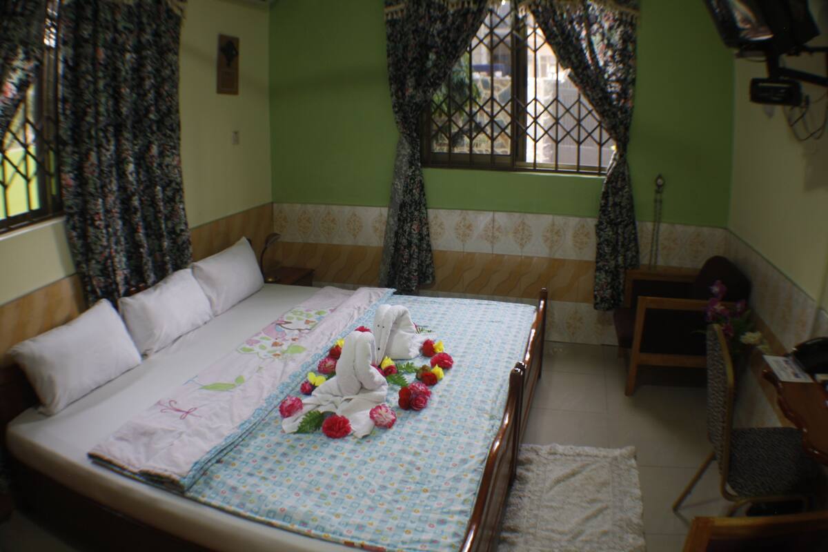 A neatly made bed with floral decorations, a wooden chair, and a small table with a vase of flowers.
