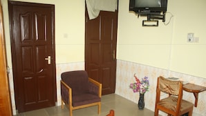 A hotel room with a bed, two wooden chairs, a small table, a television, and a vase with flowers. - Dokua Royal Hotel (Kwabenya)