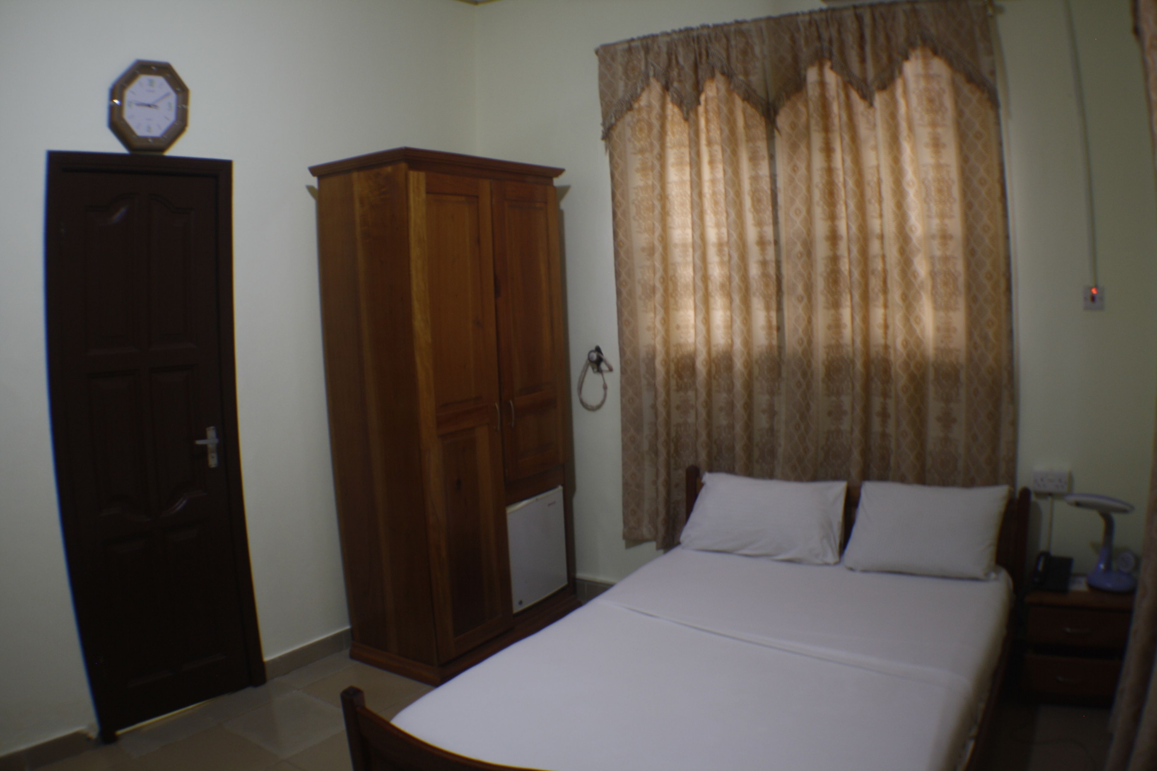 A bedroom with a bed, a wardrobe, and a window with curtains.