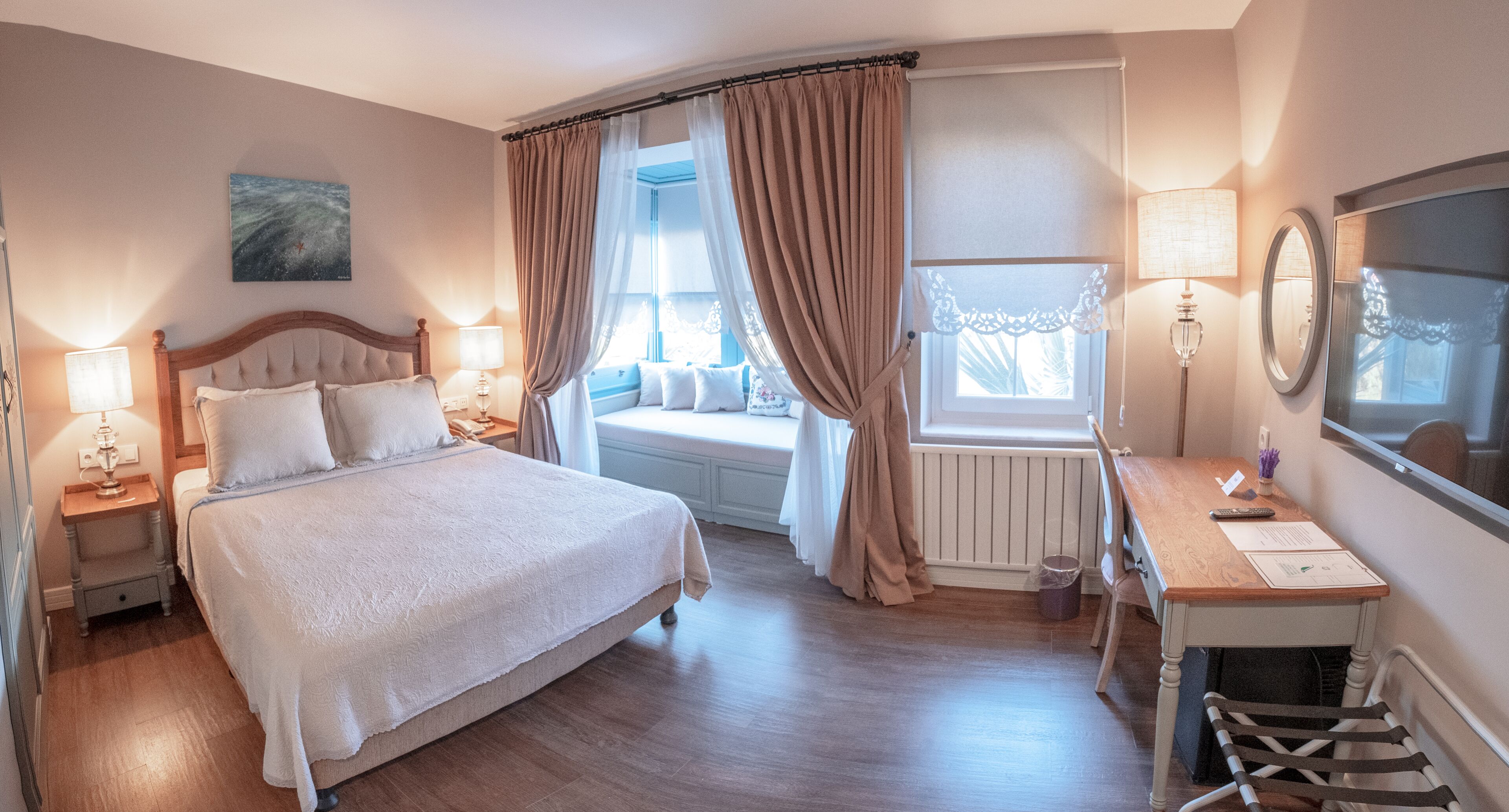 Una habitación de hotel con una cama grande, un escritorio con silla, una ventana con cortinas, un radiador y un espejo en la pared.