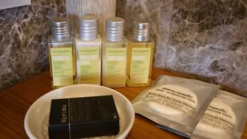 A bathroom with a marble wall, a white towel dispenser, and a set of toiletries including shower gel, body lotion, conditioner, and shampoo.