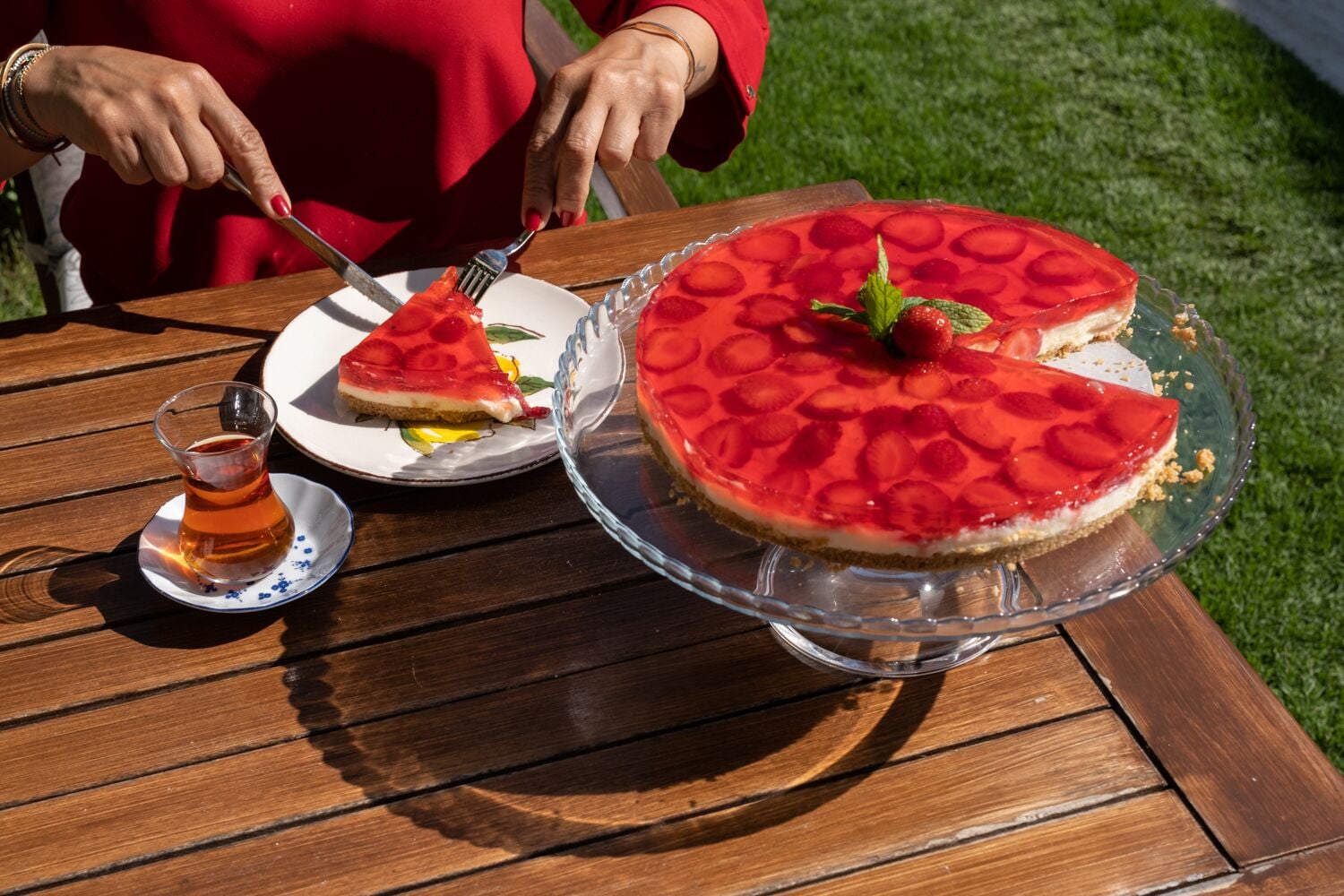 A wooden table with a large pie on a glass stand, a smaller pie on a plate, and a glass of tea.