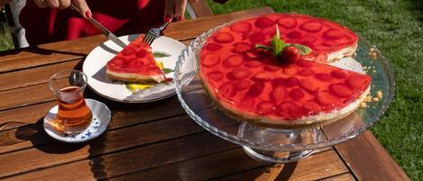 A wooden table with a large pie on a glass stand, a smaller pie on a plate, and a glass of tea.