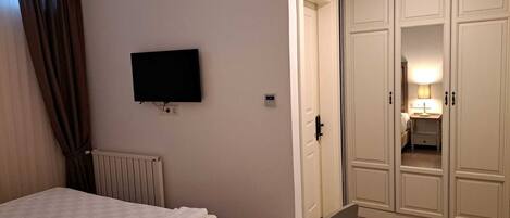 Una habitación de hotel con una cama, un televisor montado en la pared, un radiador y un armario con espejo y lámpara.
