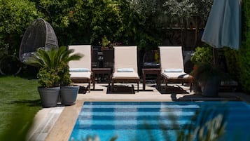 Una piscina al aire libre, sombrillas, sillones reclinables de piscina