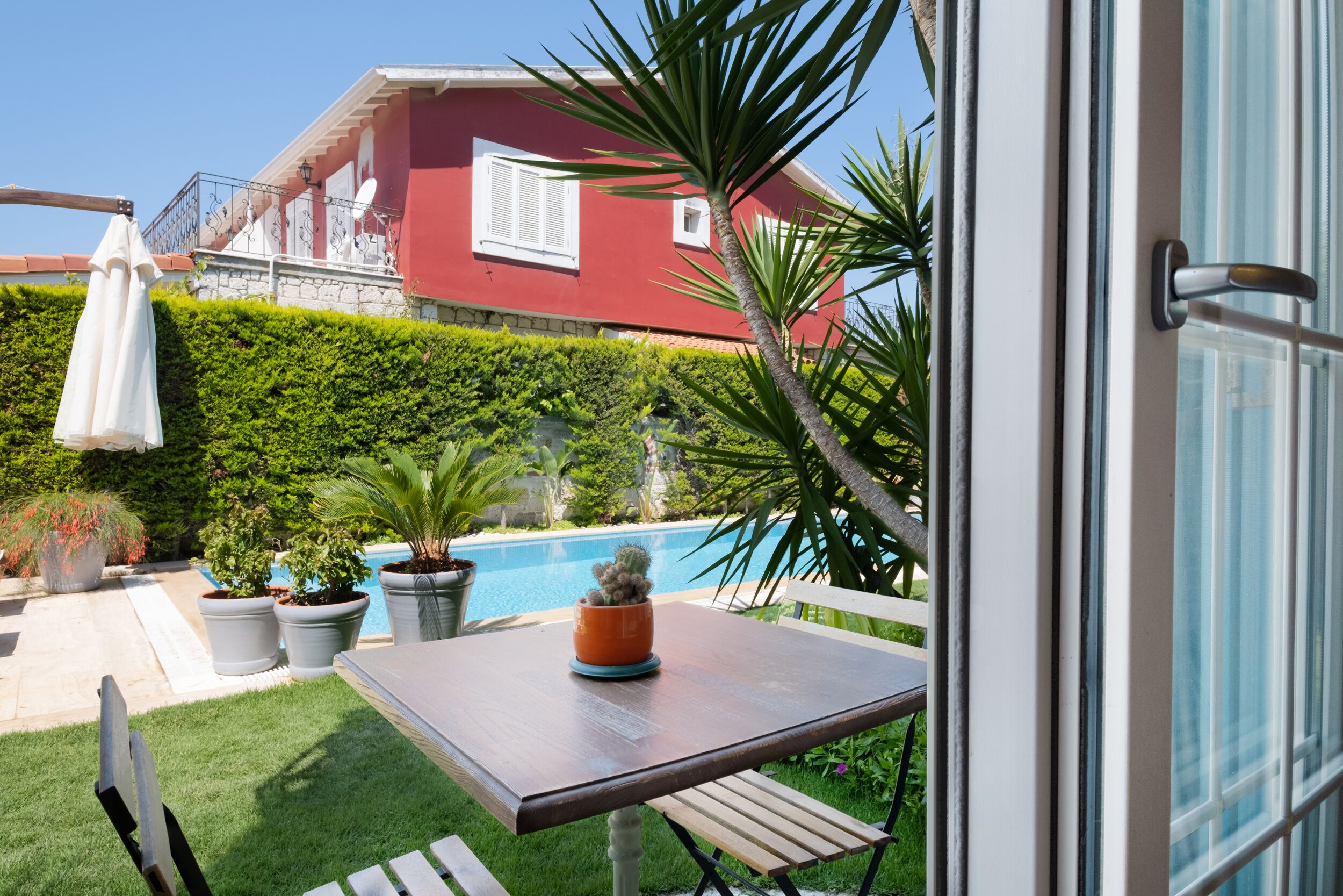 Un patio con una mesa, sillas y vistas a una piscina y un edificio rojo al fondo.