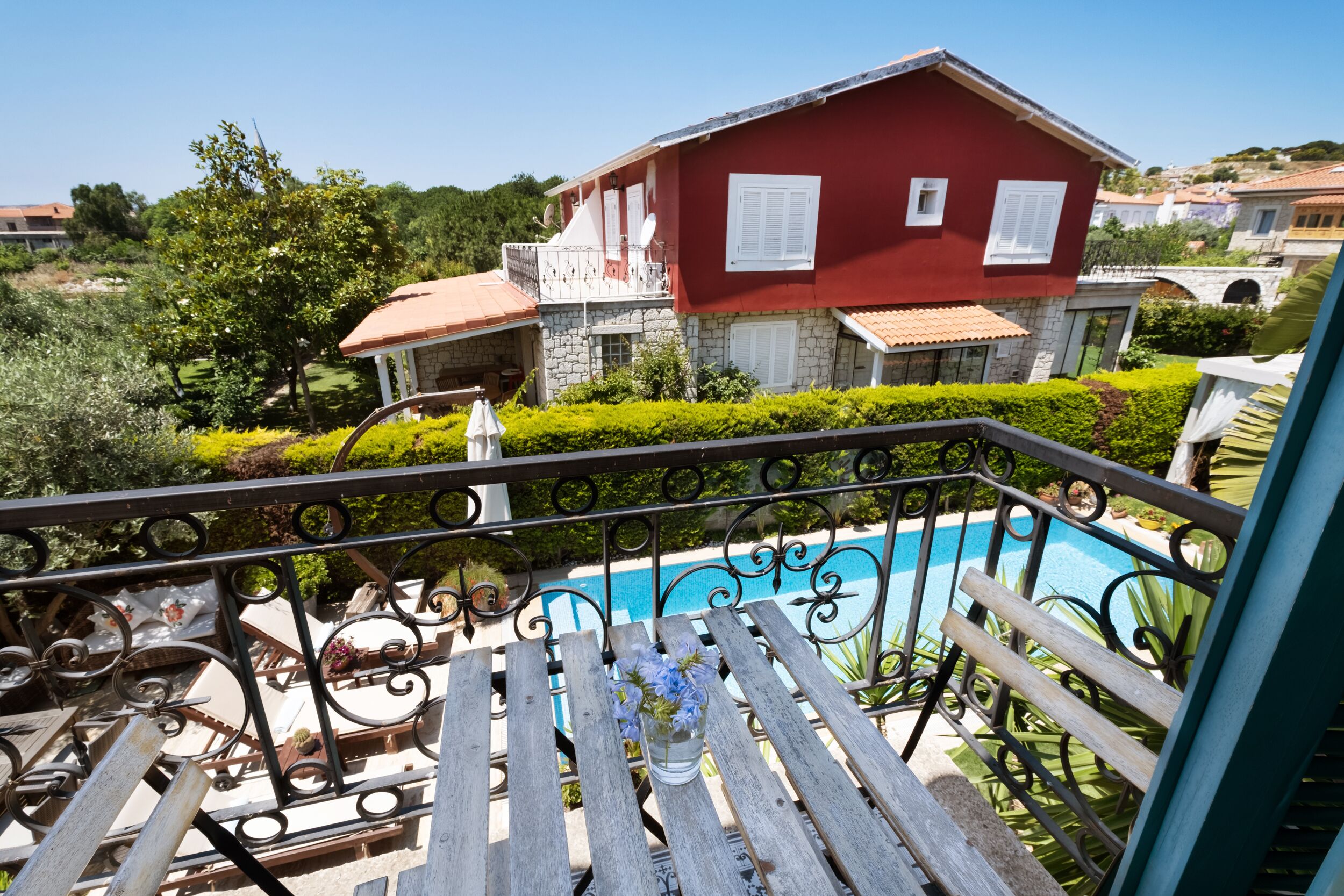 A balcony with a view of a swimming pool, a red house, and a stone building in the background.