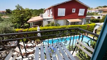 A balcony with a view of a swimming pool, a red house, and a stone building in the background.