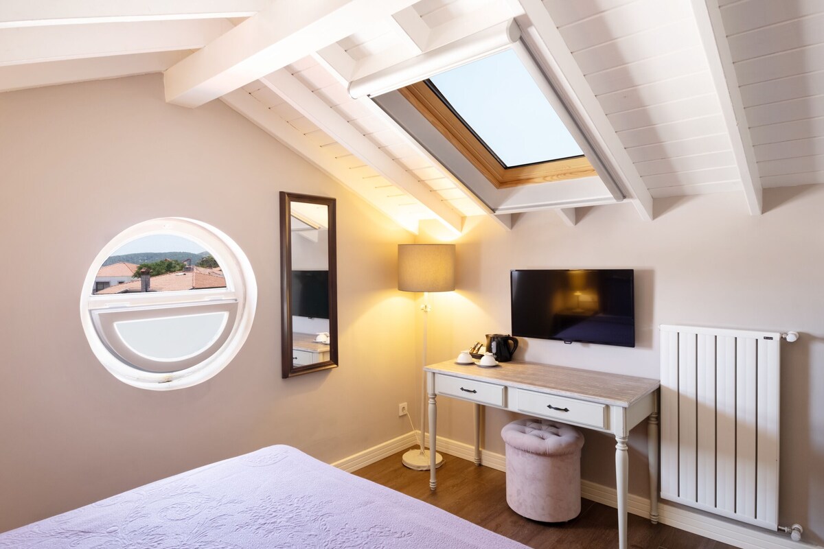 A bedroom with a skylight, a round window, a bedside table, a lamp, and a radiator.