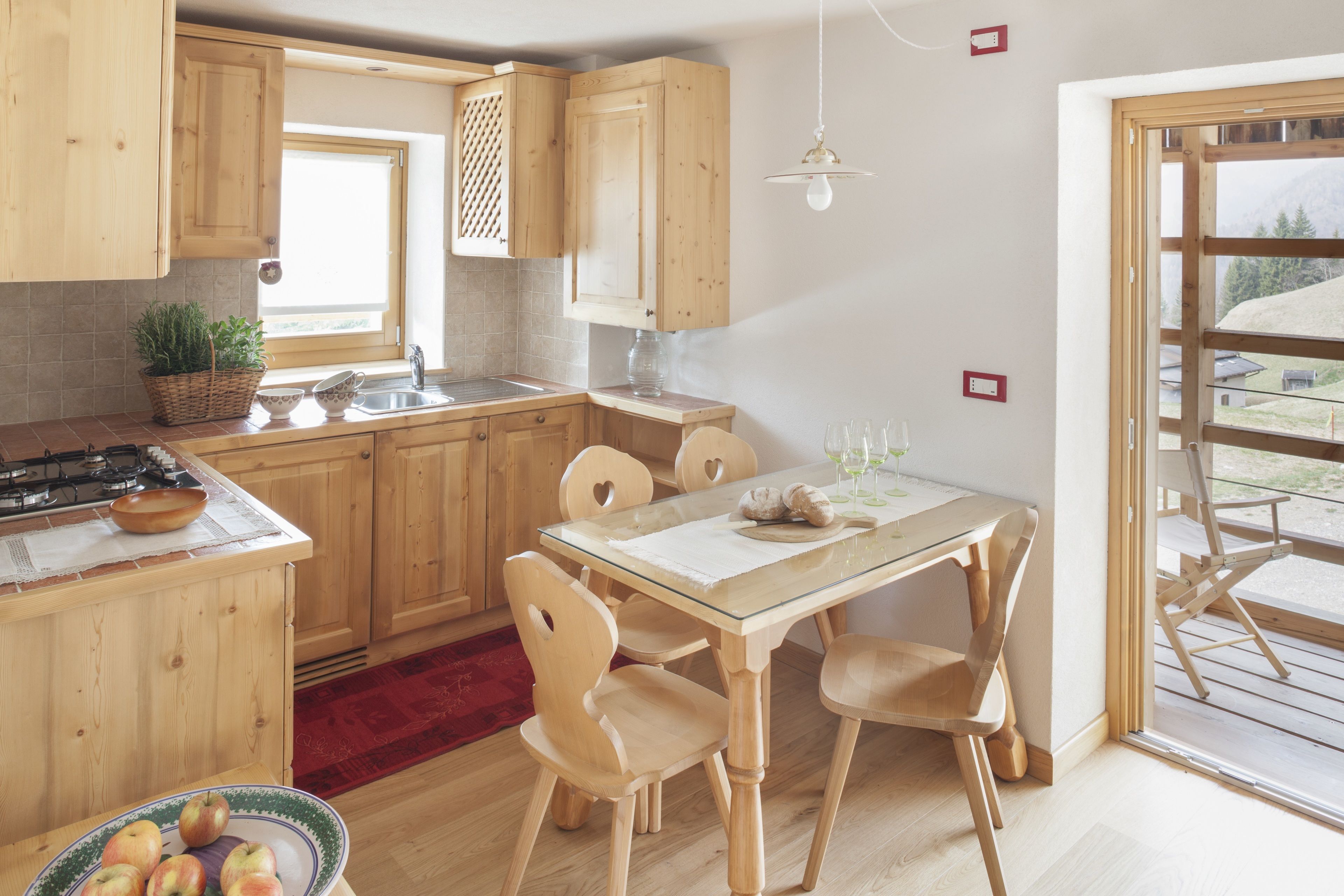 Una cocina con armarios de madera, una mesa de comedor con sillas, una alfombra roja y un ventanal con vistas al exterior.