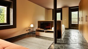 A modern hotel room with a large window, a flat-screen TV, a small round table, and a sofa.