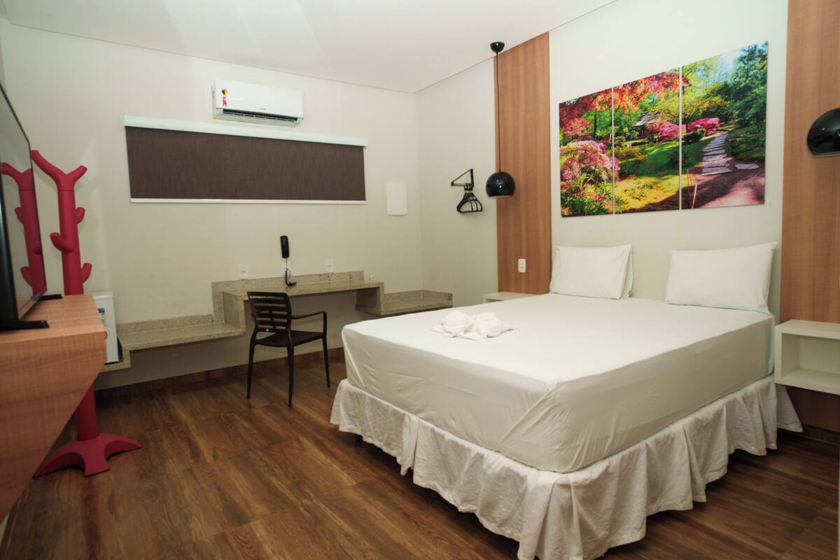 Un dormitorio con cama, escritorio, silla y un cuadro en la pared.