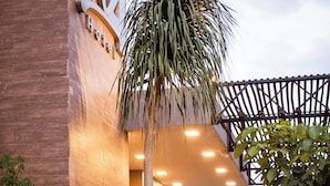 A hotel entrance with a palm tree, a covered outdoor seating area, and a tiled roof. - W4 Hotel (Irece)