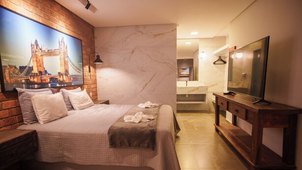 A hotel room with a large bed, a TV, a painting of a bridge, a wooden dresser, and a bathroom visible through an open door. - W4 Hotel (Irece)