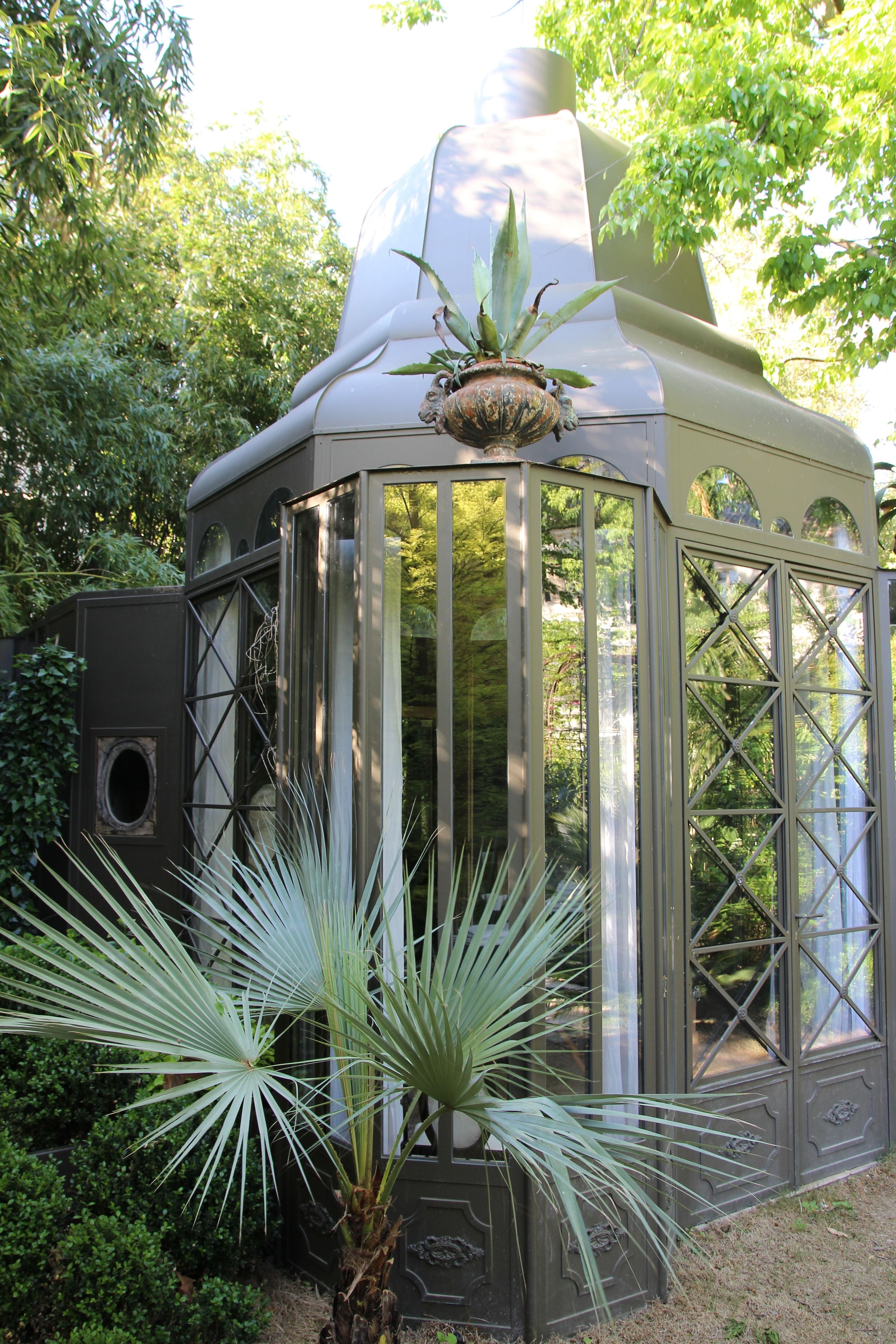 Une structure surmontée d’une coupole de verre et d’un pot de fleurs, le tout entouré de verdure.