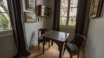 A dining area with a wooden table and chairs, framed artwork on the walls, and a window with curtains.