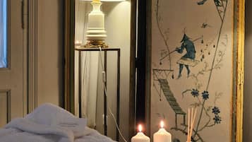Relax in a serene space with a neatly made bed, a round table with candles, and a large mirror reflecting the room's inviting decor.