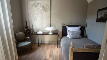 A bedroom with a bed, a chair, a desk, and a large painting on the wall.