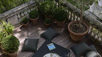 Um deck de madeira com mesa e cadeiras, cercado por plantas em vasos e vista para um jardim.