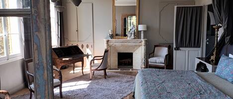 A bedroom with a bed, a desk, a chair, a fireplace, and a mirror.