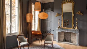 A room with two chairs, a wooden table, a fireplace, and a large mirror.