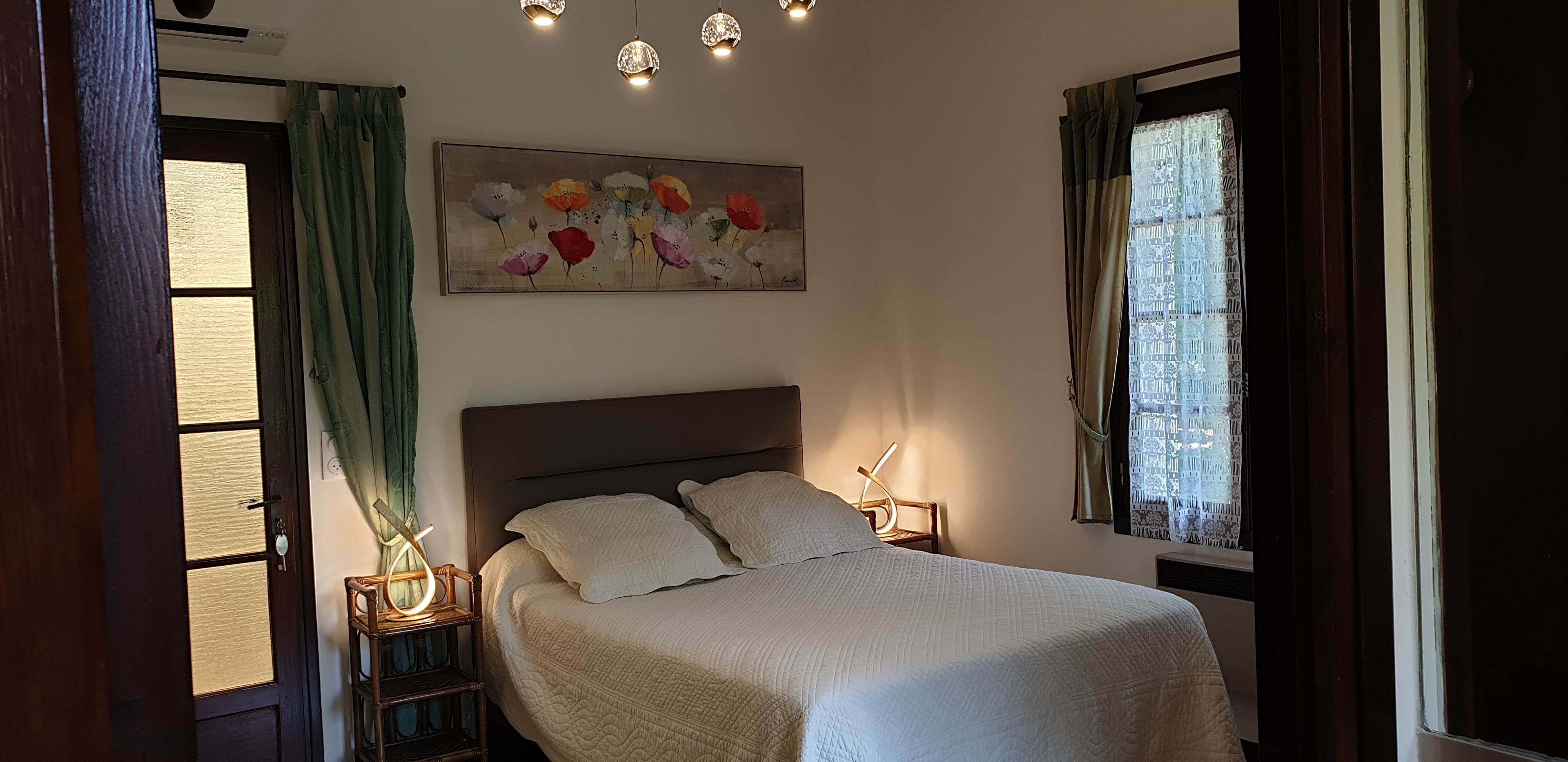 A bedroom with a bed, a painting, a nightstand, and a window with curtains.