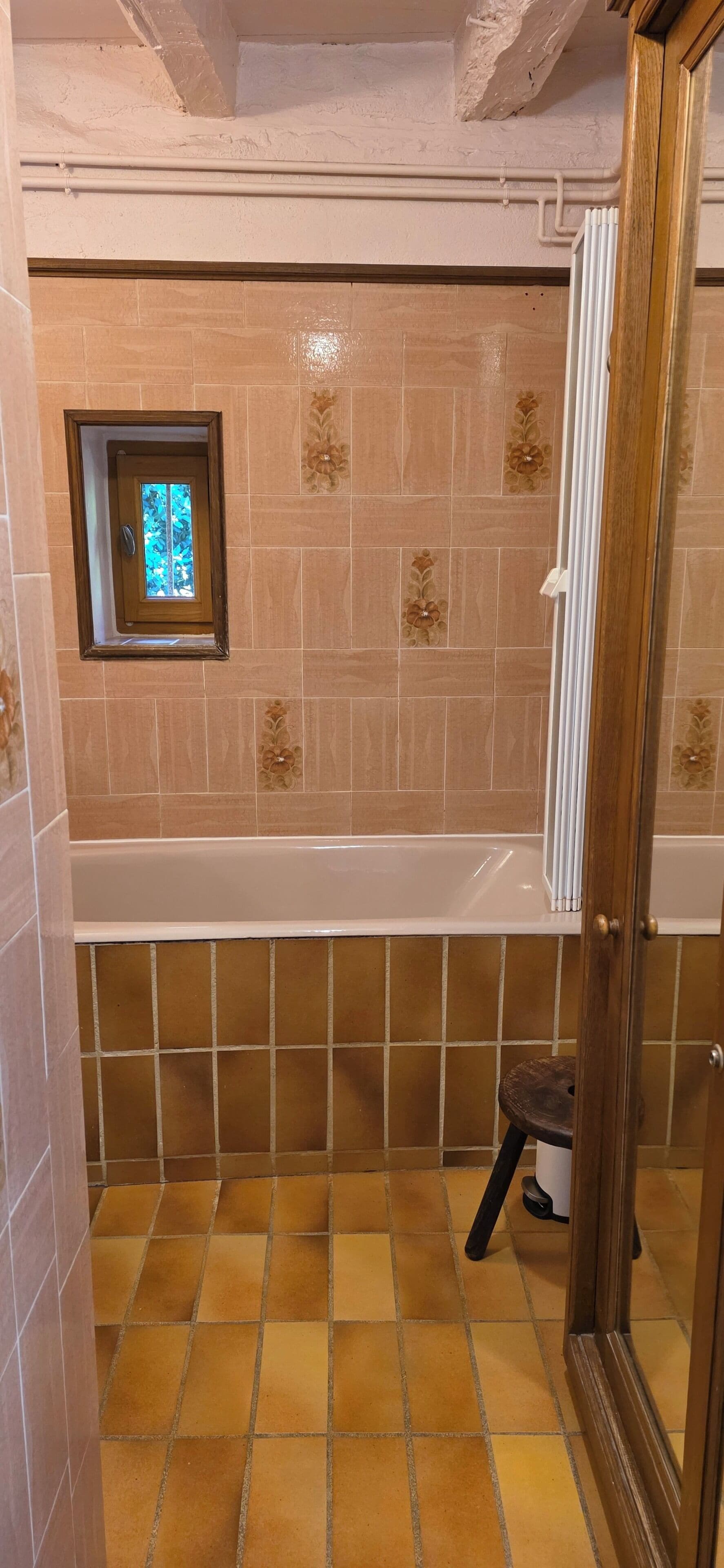 A bathroom with a bathtub, a small window, and a shower area.