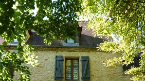 Een stenen gebouw met een houten deur, twee ramen met luiken en treden die naar de ingang leiden.