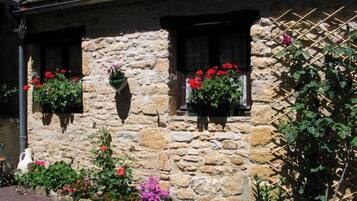 Un bâtiment en pierre doté de trois fenêtres, chacune ornée d’une jardinière contenant des fleurs rouges et roses.