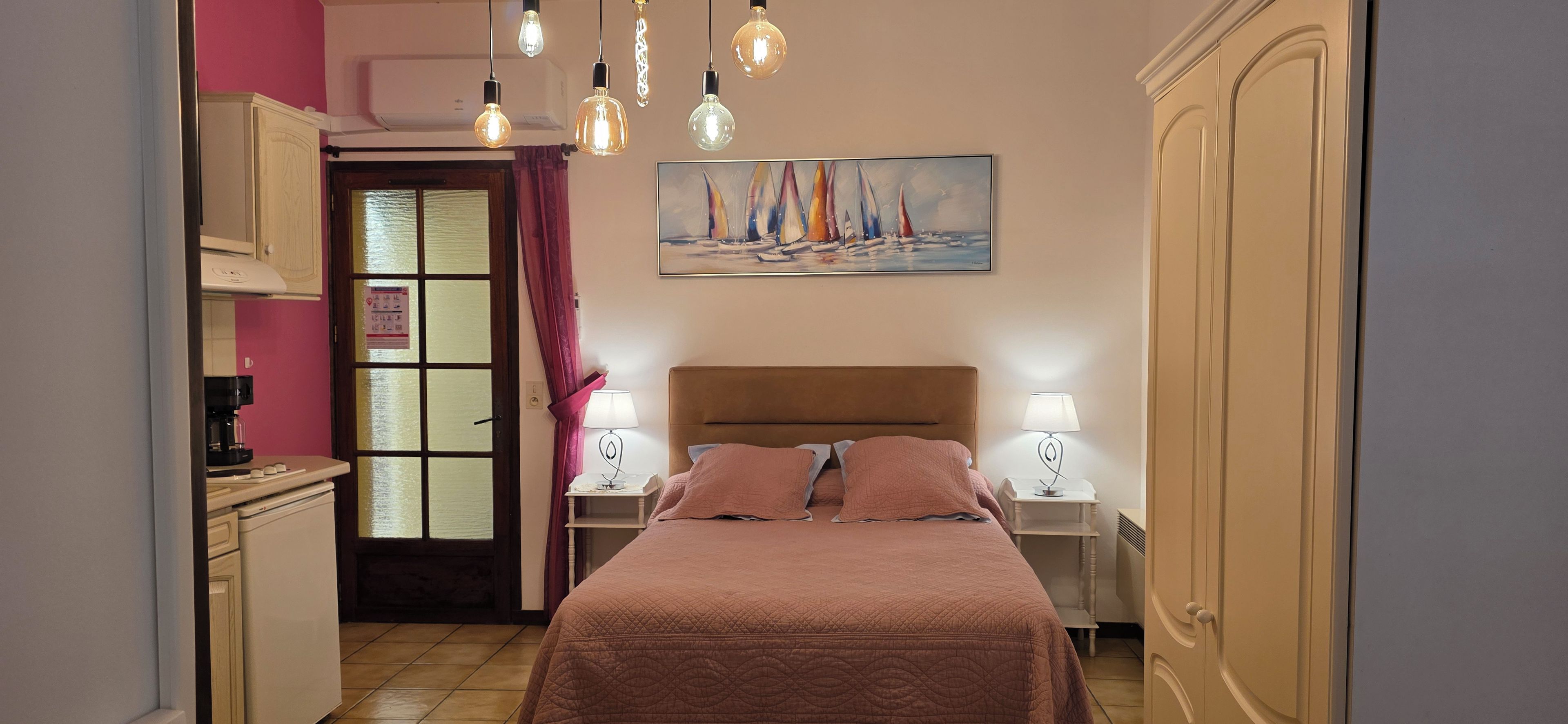 A bedroom with a bed, two bedside tables with lamps, a painting above the bed, and a door with a glass panel.