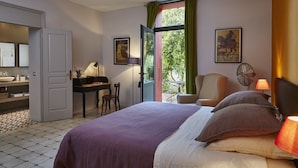 A hotel room with a bed, a desk, a chair, a table, and a window with curtains. - Clos des Aspres (Ortaffa)