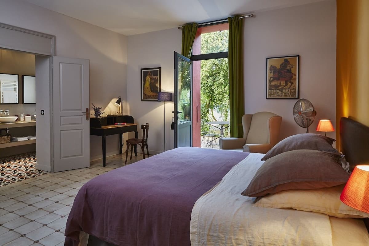 A hotel room with a bed, a desk, a chair, a table, and a window with curtains.
