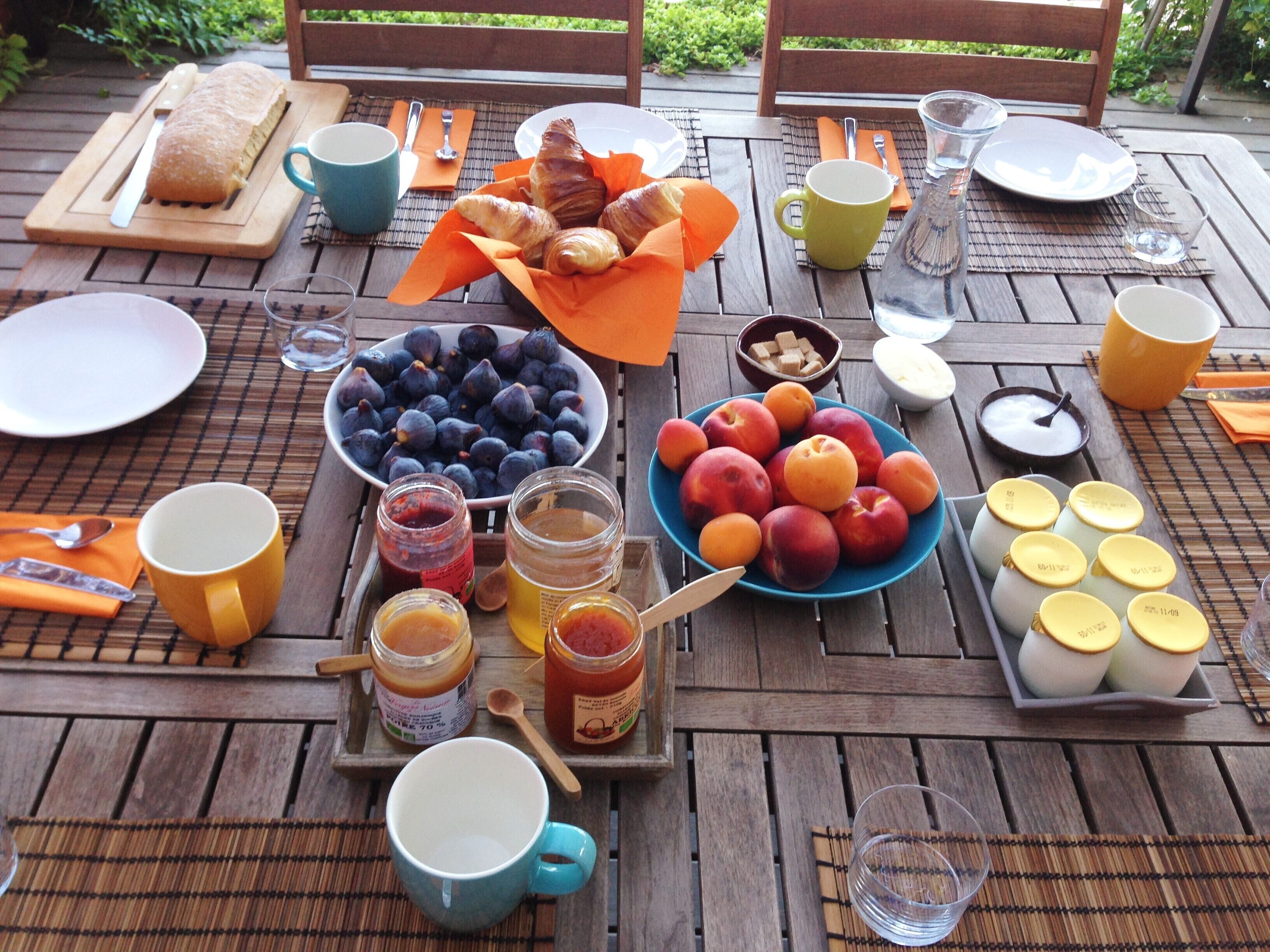 Una mesa de madera con comida, bebidas y utensilios para un picnic.