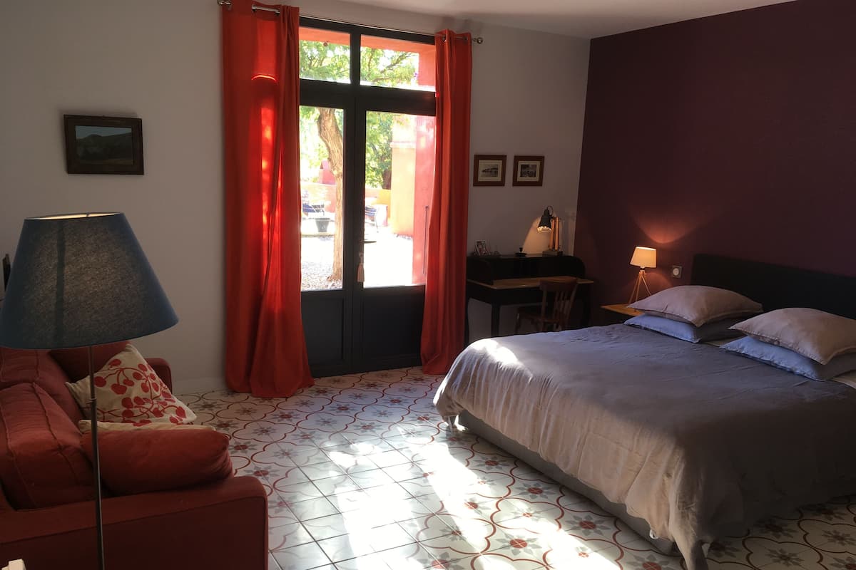 A bedroom with a bed, a desk, a chair, a lamp, and a window with curtains.