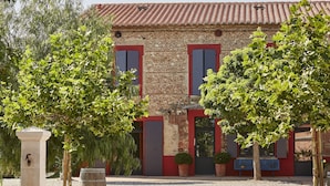 A building with a stone facade, red shutters, and a gravel courtyard. - Clos des Aspres (Ortaffa)