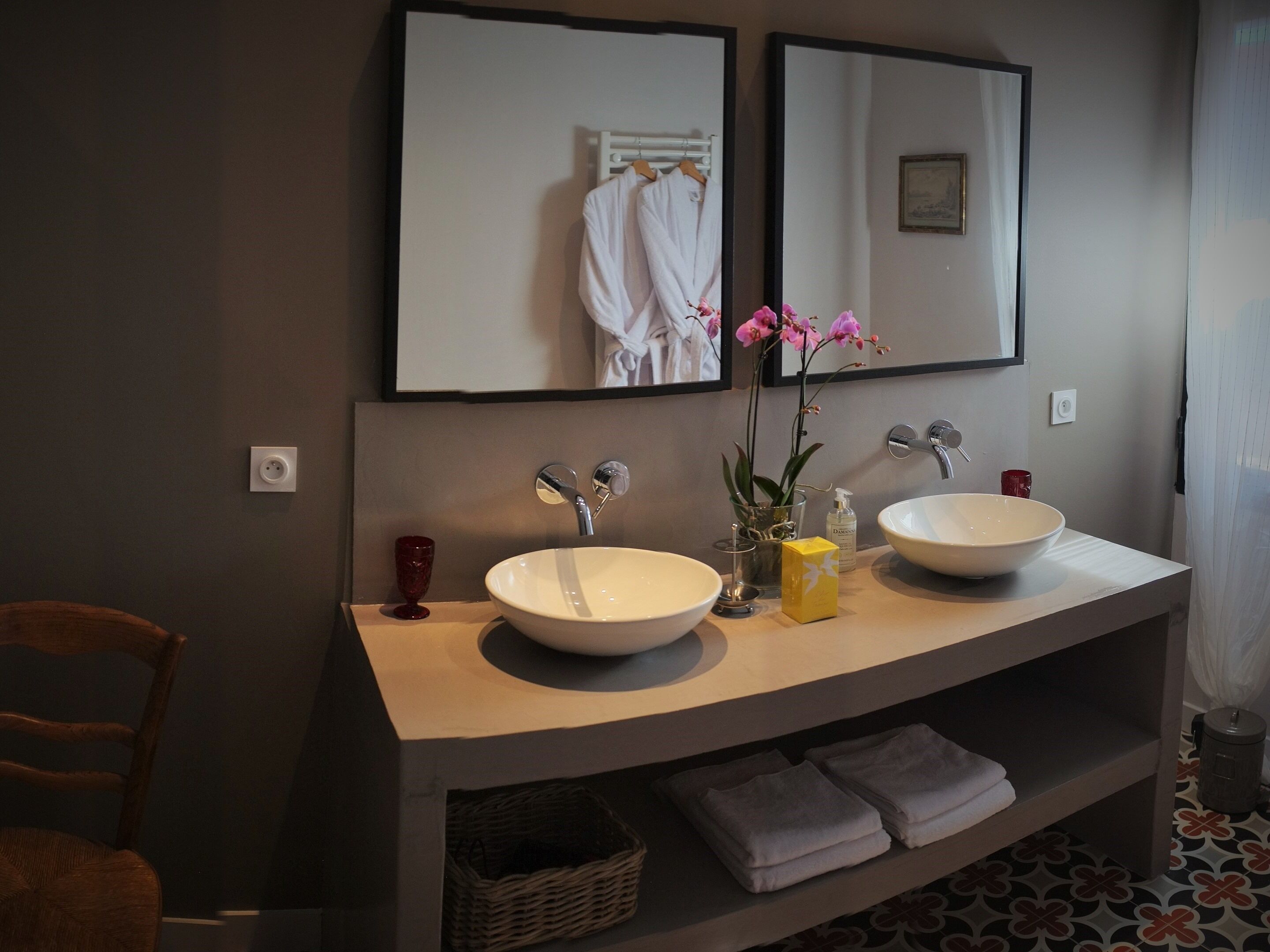 A bathroom with two sinks, a mirror, a towel rack, and a shelf with folded towels.