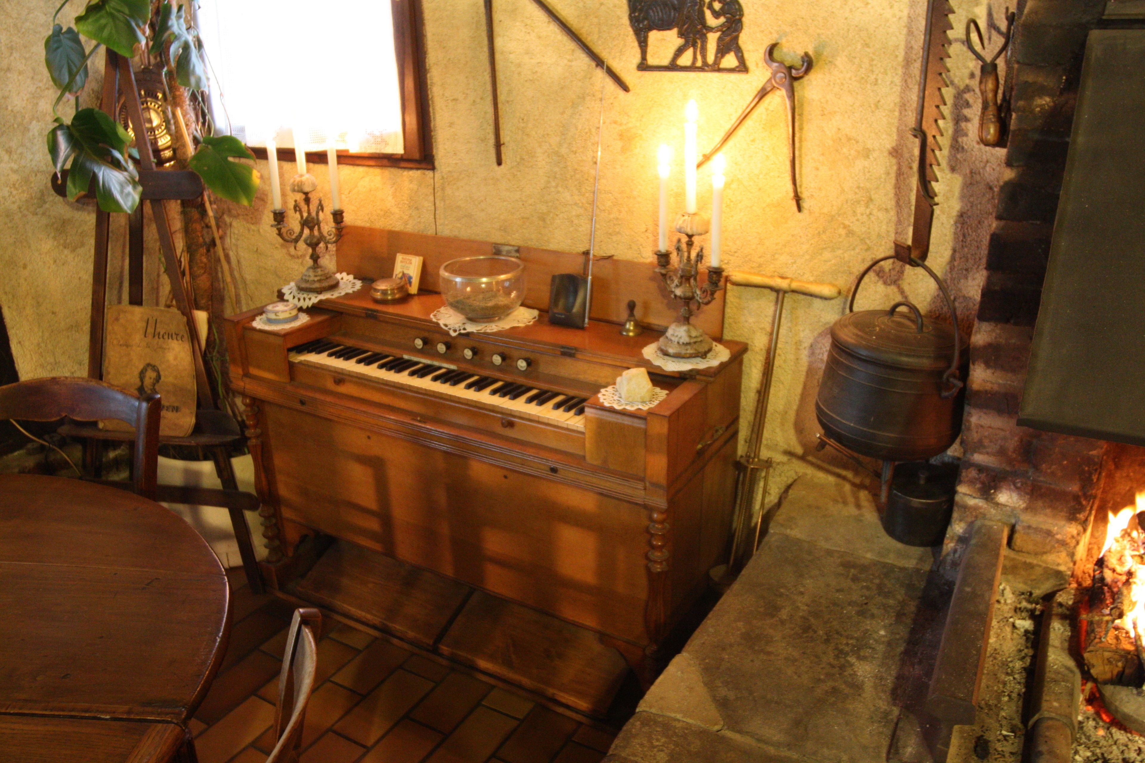 Een gezellige kamer met een houten piano, een tafel, stoelen, een kandelaar en een open haard.
