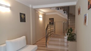 A modern interior with a white sofa, a staircase, and a potted plant. - Palazzo Ducale (San Severo)