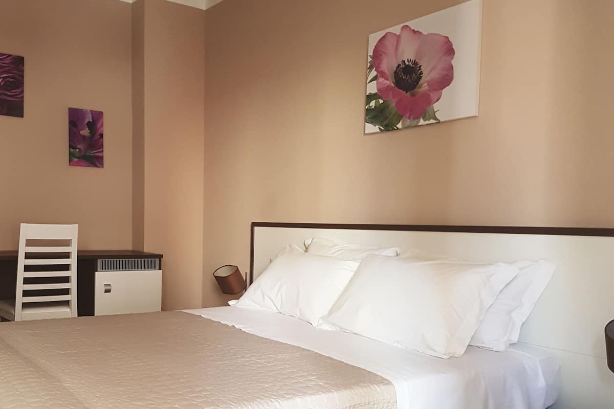 A bedroom with a large bed, a nightstand, a chair, and a wall-mounted lamp.