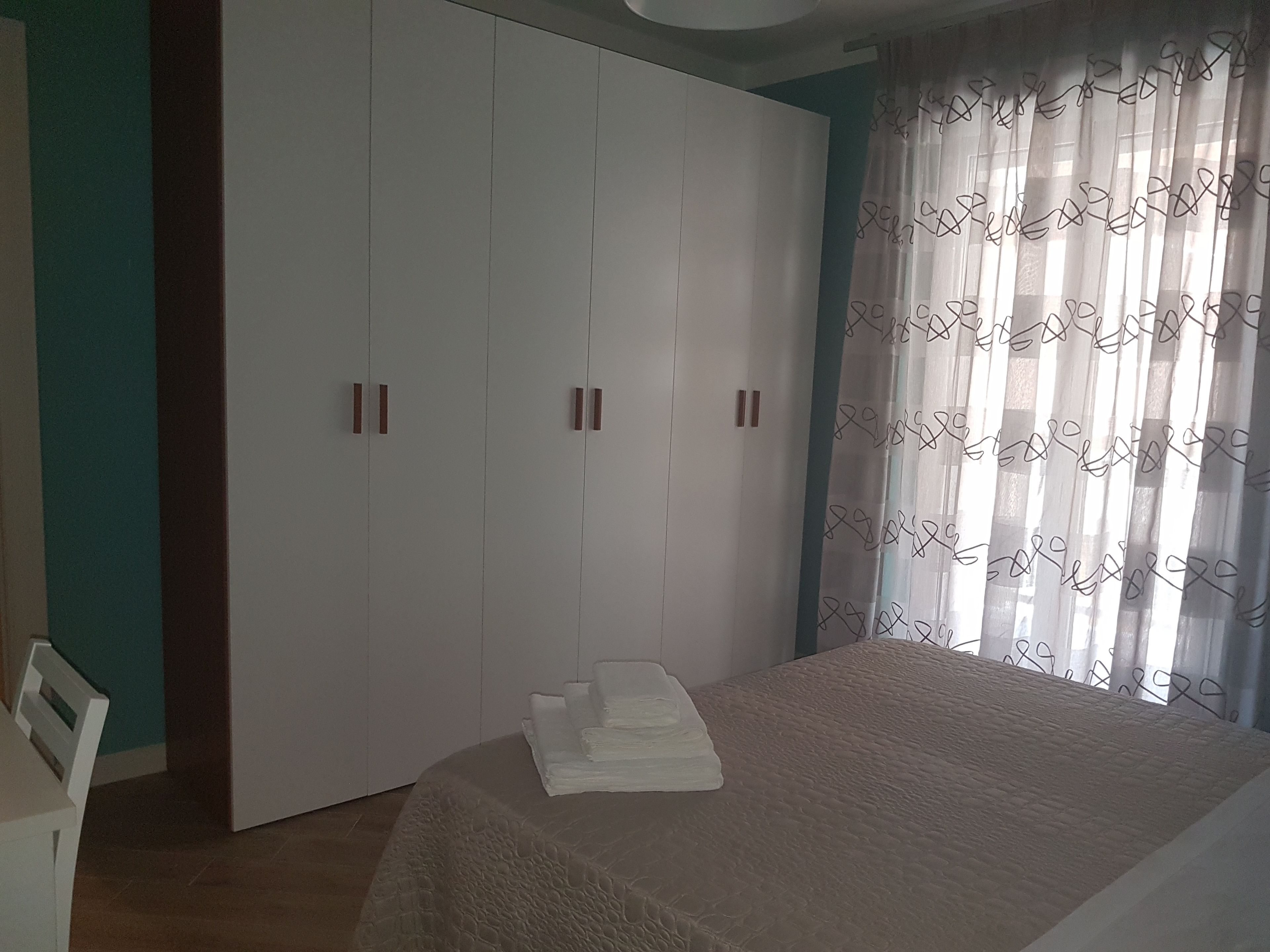 A bedroom with a bed, a wardrobe, and a window with curtains.