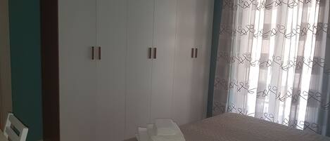 A bedroom with a bed, a wardrobe, and a window with curtains.