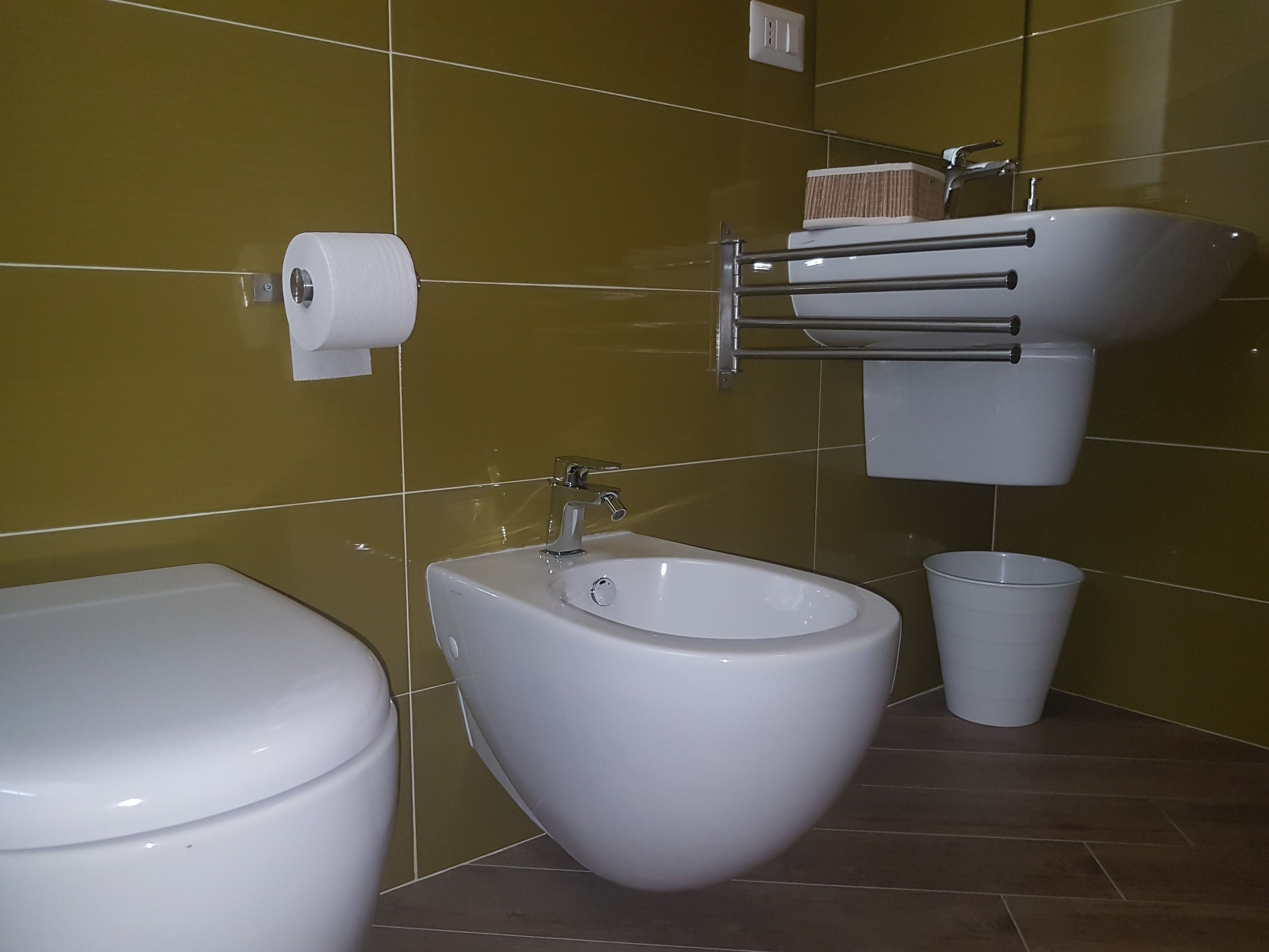 A bathroom with a toilet, bidet, sink, and a trash bin.