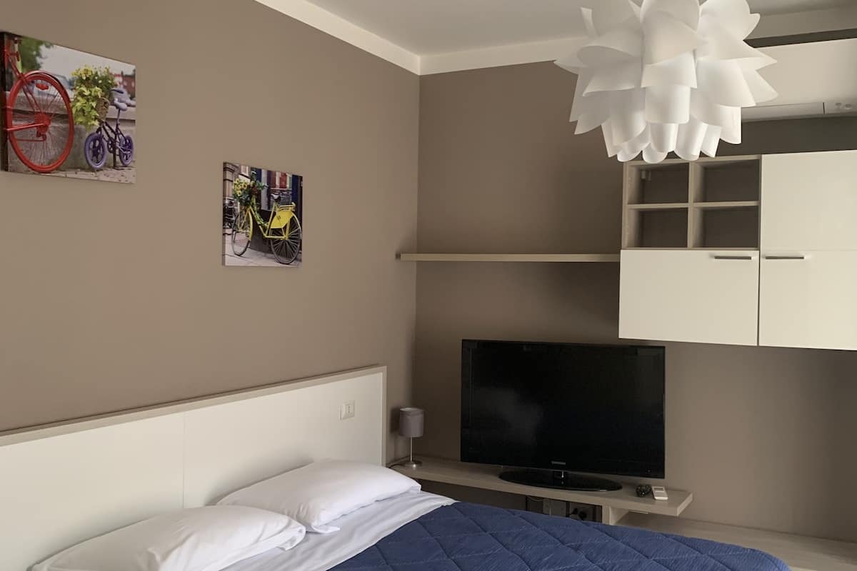 A bedroom with a bed, a TV, a white wardrobe, and a wall-mounted light fixture.