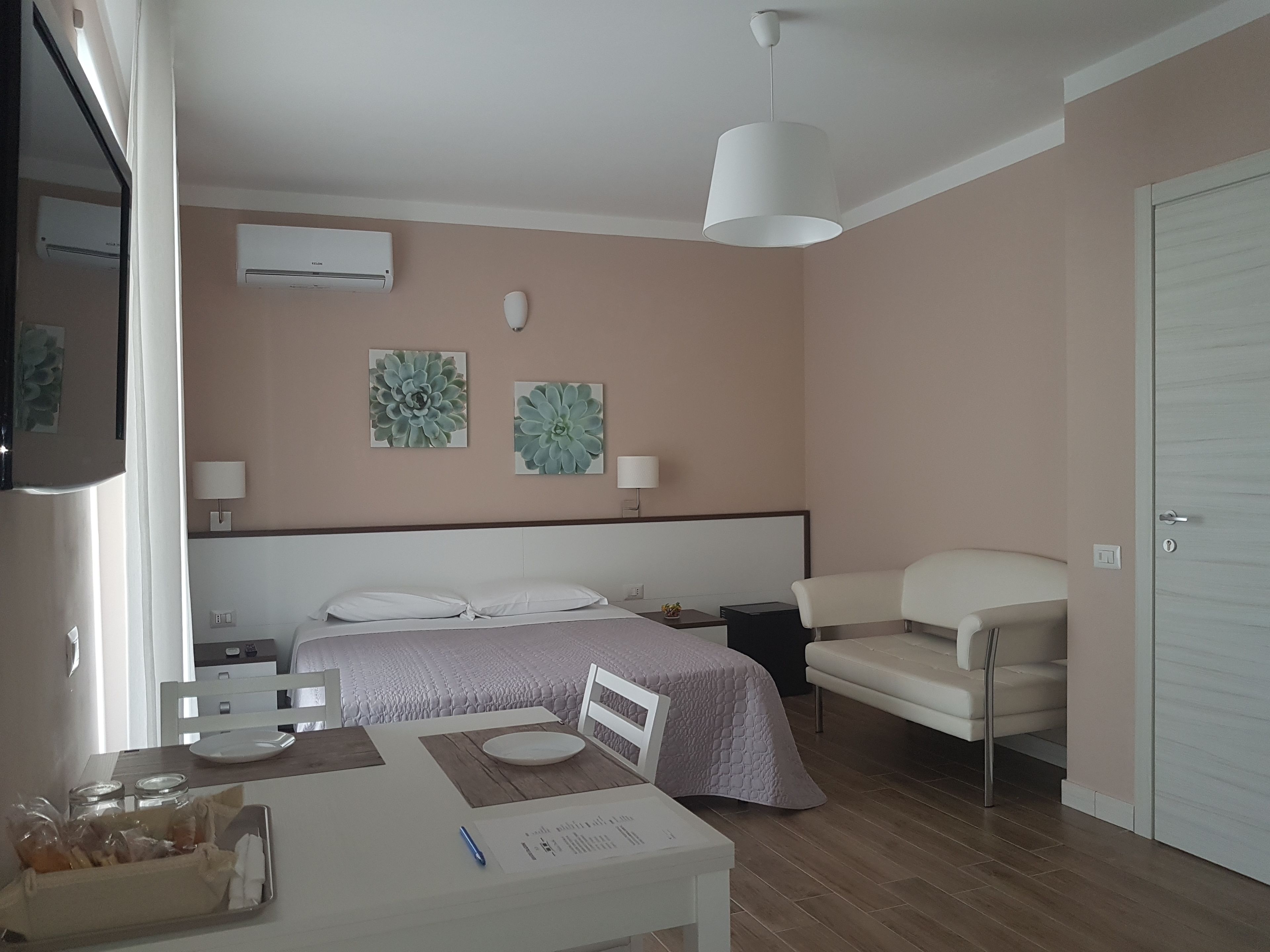 A hotel room with a bed, bedside tables, a desk with a chair, a white lamp, and artwork on the wall.