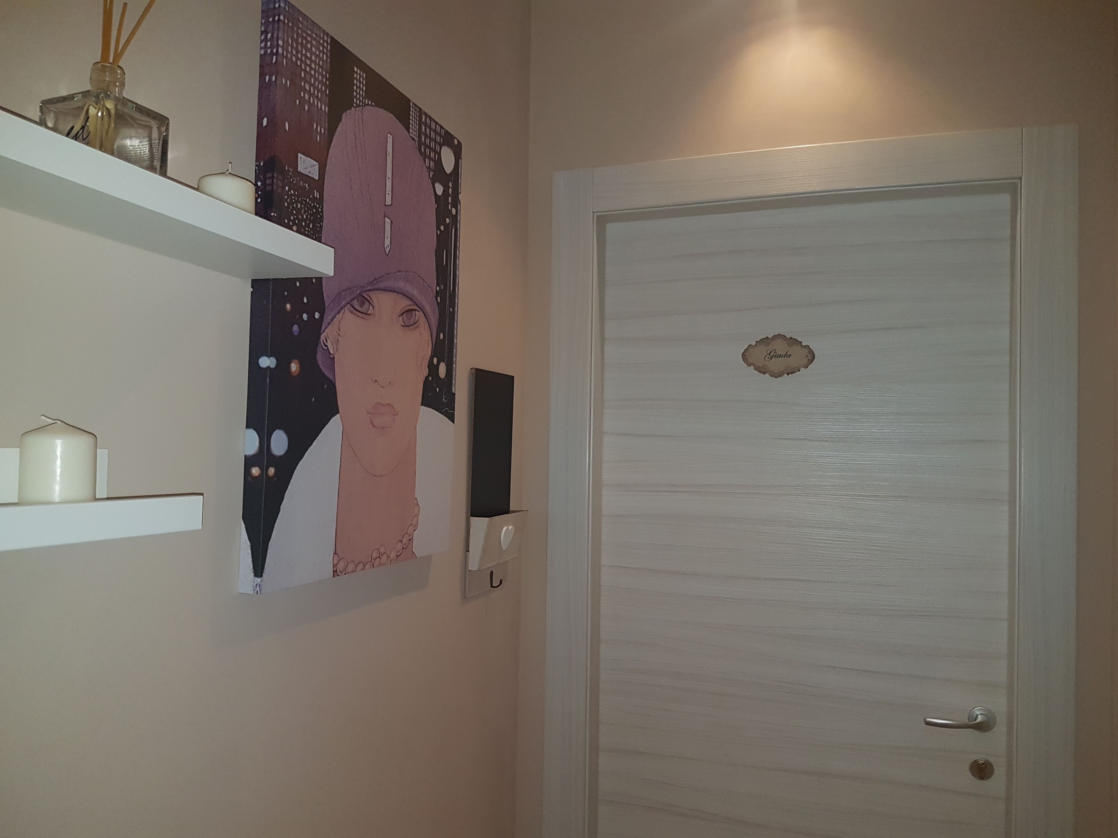 Una puerta blanca con una placa, una obra de arte colgada en la pared y una repisa con velas.