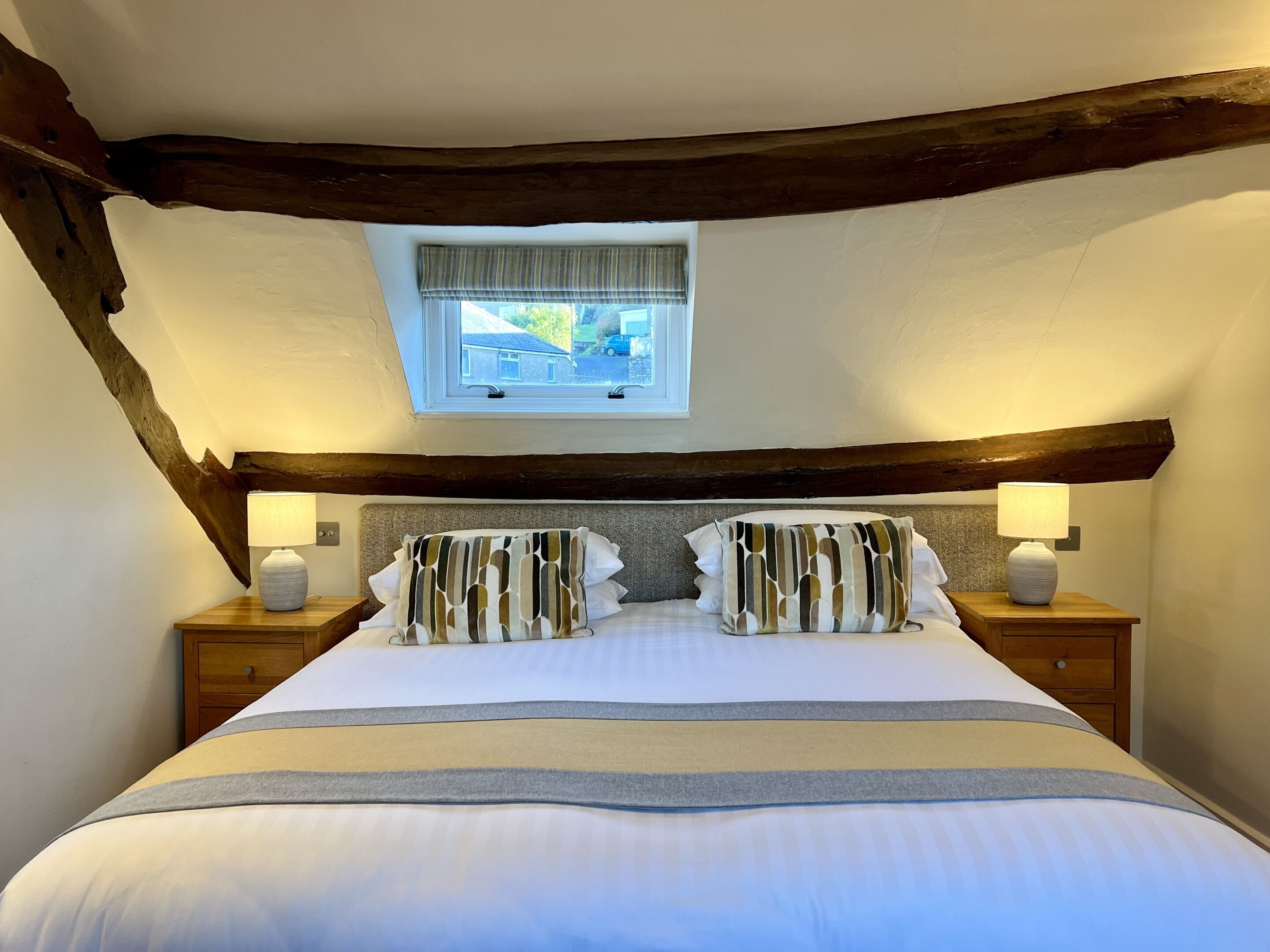 Un dormitorio con una cama grande, vigas de madera, un tragaluz y lámparas de noche.